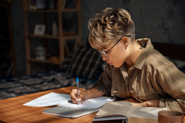 Education. Young woman short hair in glasses sitting at desk studying reading book taking notes concentrated close-up stock photo