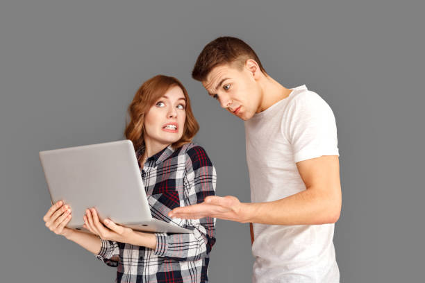 istock Freestyle. Young couple standing isolated on grey with laptop concerned with website content 1200003706