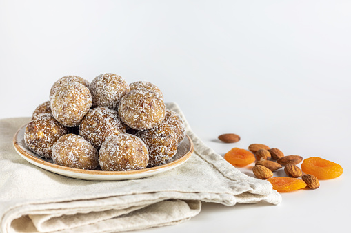 Homemade energy balls with dried apricots, raisins, dates, prunes, walnuts, almonds and coconut. Healthy sweet food. Energy balls in a plate on a white background.