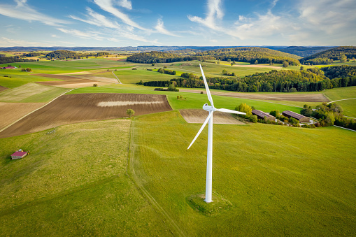 Drone point of view towards modern wind turbine surrounded in rural green natural landscape on a sunny late summer day. Green Energy, Alternative Energy Environment Concept Shot. Baden Württemberg, South Germany, Europe