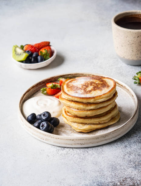 istock Delicious breakfast - stack fritters pancakes, sprinkled with powdered sugar with fruits and berries and sour cream on plate on wood table. 1200048816