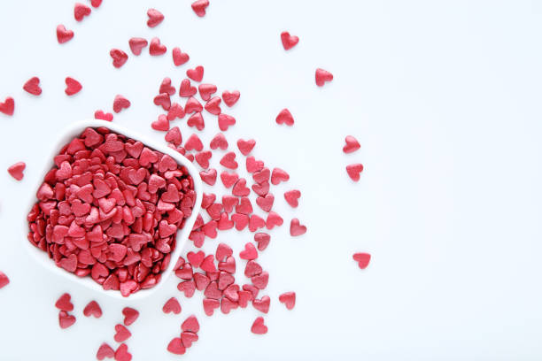 Red heart shaped sprinkles in bowl on white background