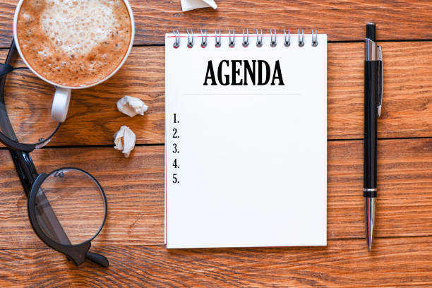 istock Agenda text in an office notebook and wooden table. Top view, high resolution photography. 1200063708