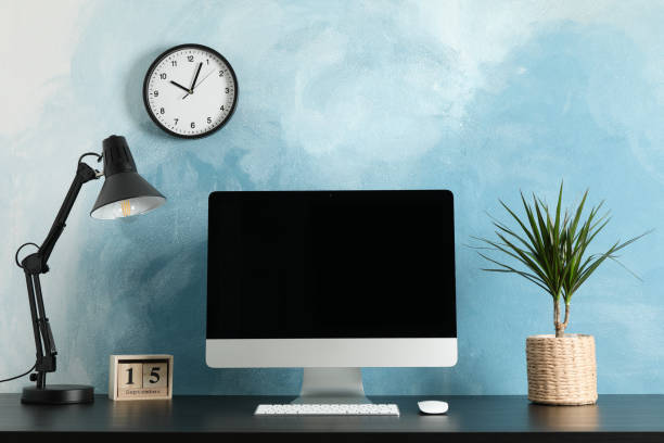istock Workplace with computer, plant and lamp on wooden table. Light blue background 1200063772