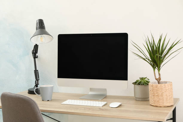 istock Workplace with computer, plants and lamp on wooden table. Empty black screen 1200064469