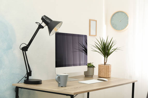 istock Workplace with computer, plants and lamp on wooden table. Empty black screen 1200064539