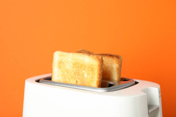 istock Toaster with bread on grey table against orange background, close up 1200067426