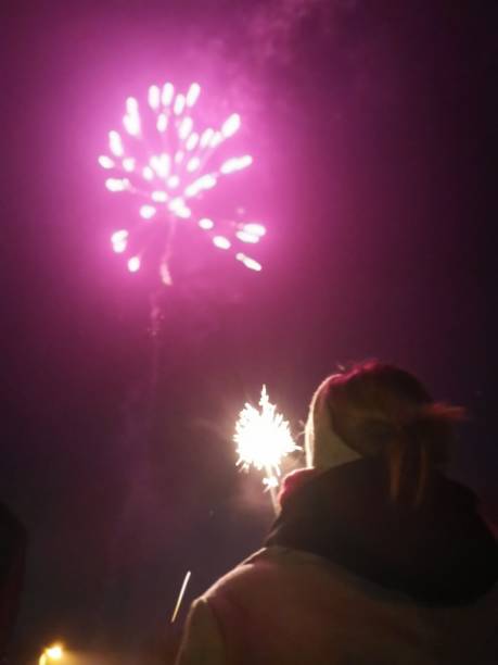 istock Vertical image of young woman watching a firework while holding a sparkler in her hand 1200075624
