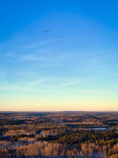 Mountaintop view of trees, bright colored sky and a small airplane in sky stock photo