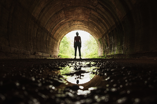 A young woman standing at the end of a tunnel and her reflection on a puddle