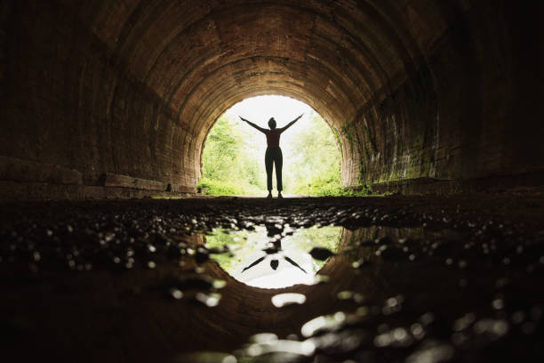 jeune femme avec des bras levés et son reflet à l'intérieur d'un tunnel - apercevoir le bout du tunnel photos et images de collection