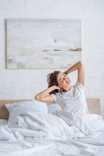 istock dreamy girl smiling while touching hair in bed 1200078971
