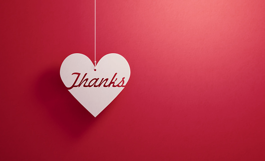 Thanks written white heart shape hanging over red background, Horizontal composition. Thank you concept.