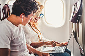 Happy travelers couple mother and son sit down on the airplane ready to enjoy the flight with personal computer laptop with internet connection on board - modern technology and travel people concept
