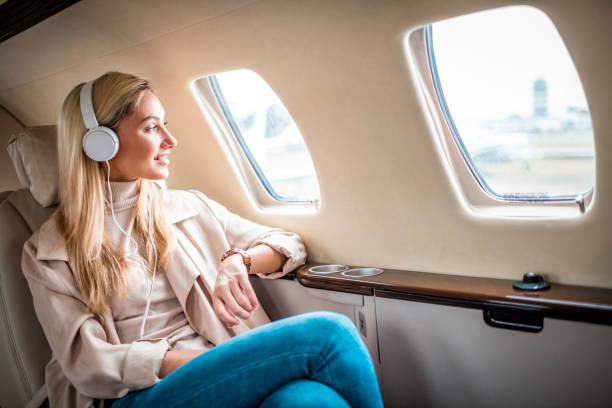 Young businesswoman traveling with a private airplane Young successful woman sitting on a private jet and listening to music through headphones. vehicle interior audio stock pictures, royalty-free photos & images