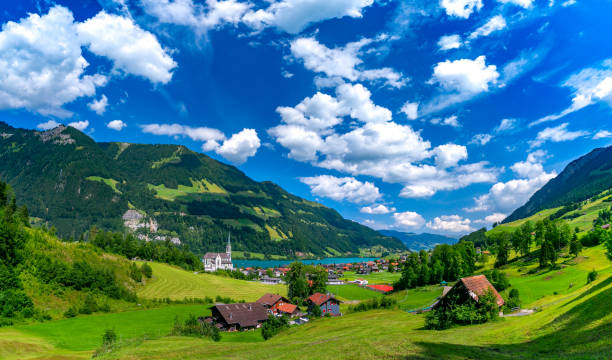 Panorama of swiss village Lungern with church and traditional wood houses on lake Lungernsee in sunny summer day, Obwalden, Switzerland