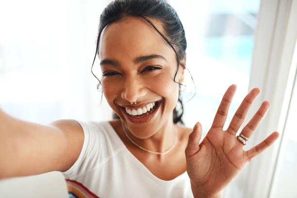 Hi everyone, welcome back to the channel! Cropped portrait of an attractive young blogger standing in her home and waving at the camera during a selfie self portrait stock pictures, royalty-free photos & images