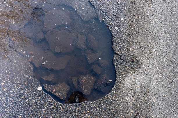 istock road pothole flooded with board water, close-up. Background texture 1200088552