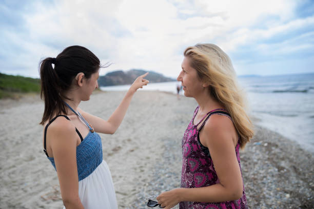 Mother and her daughter walking on the windy beach.The daughter wears hearing aids and points her finger toward the open sea