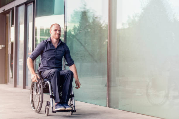 istock Man in a wheelchair rolling past a modern office building 1200091267