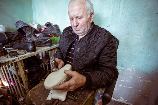 Craftsman in an old messy studio repairing men and women shoes with his tools and hands