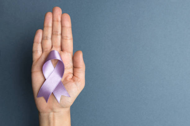 Directly above view of a hand holding purple awareness ribbon over blue background. 
Some issues for what the purple awareness ribbon stands for are Alzheimer’s Disease, Animal Protection, Bulimia Nervosa, Chronic Pain, Dementia, Diabetic Neuropathy, Domestic Violence, Drug Overdose, Homelessness, Pancreatic Cancer, Vitiligo, Thoracic Outlet Syndrome, Lupus and International Women’s Day.