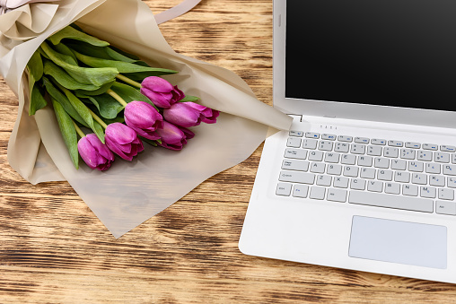 Bouquet of tulips and laptop on wooden table