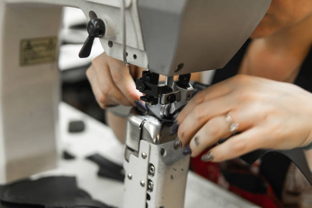istock Sewing machine in a leather workshop in action with hands working on a leather details for shoes. Women's hands with sewing machine at shoes factory. 1200104644