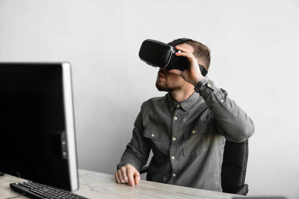 istock Young bearded man sitting against computer with virtual reality glasses. Modern technologies. The concept of future technology. 1200106153