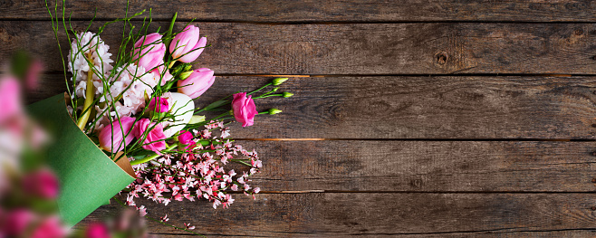 Bouquet of pink spring flowers with easter egg on old rustic boards. Flat lay floral decoration for an Easter background. Horizontal top view with space for text and design.