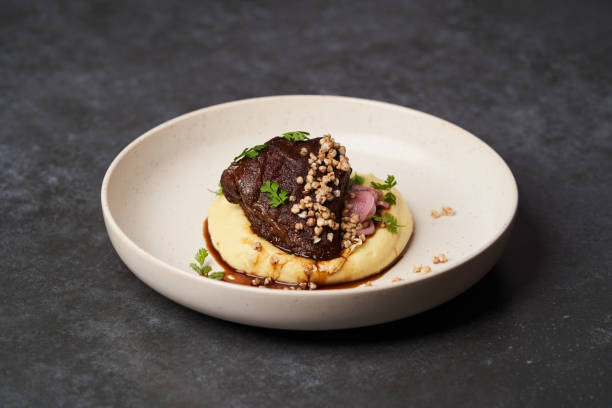 istock Stewed veal cheeks with mashed potatoes on a white plate, close-up. 1200111990