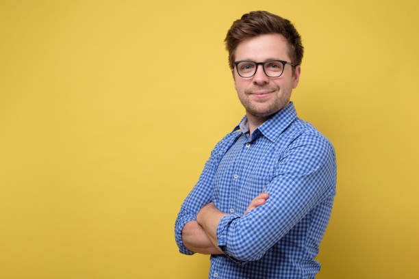 istock Handsome young man with folded hands smiling against yellow background 1200112420