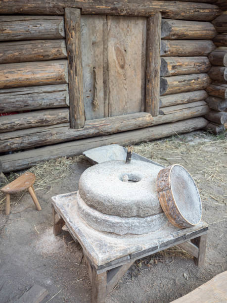 istock Rotary discoid mill stone for hand-grinding a grain into flour. Medieval hand-driven millstone grinding wheat. The ancient Quern stone hand mill with grain near log house or russian izba 1200116453