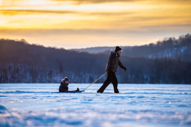 avô que puxa o neto no trenó no lago congelado no inverno no por do sol - recreational equipment - fotografias e filmes do acervo