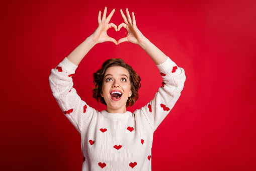 Portrait of astonished girl make heart hands enjoy passionate love sign look impressed, scream wow omg wear white jumper isolated over shine color background