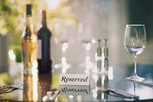 Restaurant reserved table sign in sunslight with place setting and wine glasses ready for a party