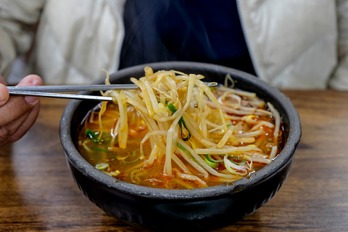 Close up  Asian woman traveller eating Korean vegetable soup with rice & bean sprouts  (sogogi gukbap)
