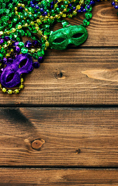 Mardi Gras masks, jewellery and trinkets Mardi Gras masks and trinkets, garlands, beads, dice and chains. Close-up on a wooden background purple and gold masquerade masks stock pictures, royalty-free photos & images