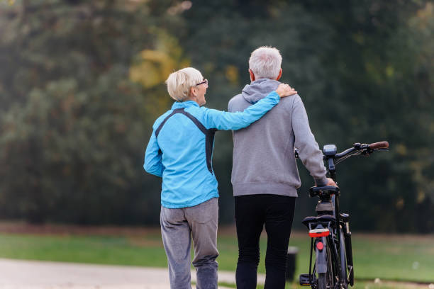 istock Cheerful active senior couple with bicycle walking through park together 1200129255