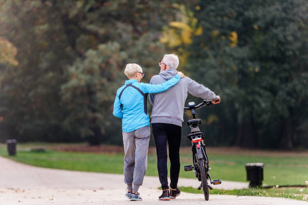 istock Cheerful active senior couple with bicycle walking through park together 1200129260