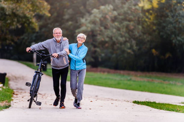 istock Cheerful active senior couple with bicycle walking through park together 1200129430