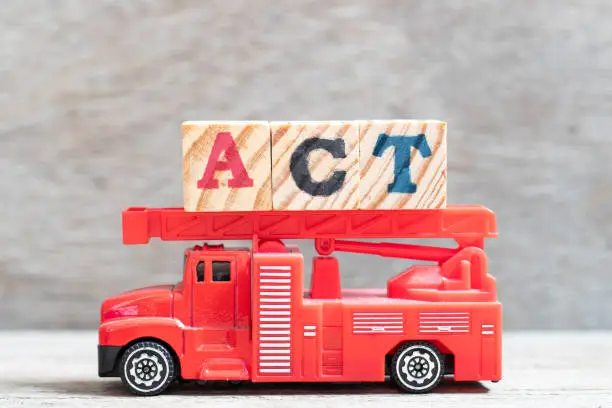 Red fire truck hold letter block in word act on wood background