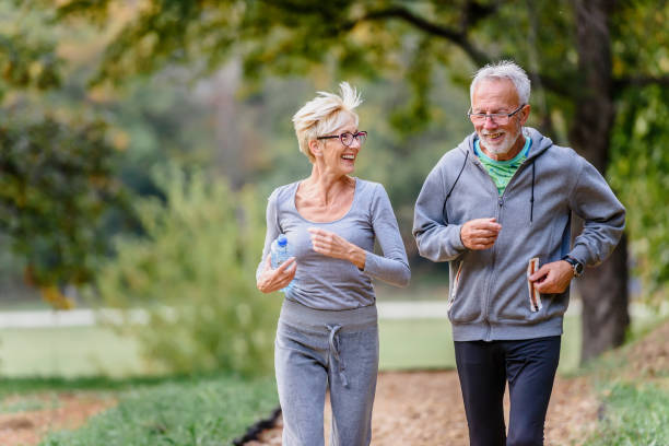 fröhliches aktives seniorenpaar joggt morgens im park - alterungsprozess stock-fotos und bilder