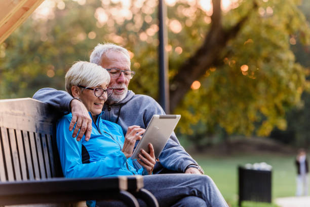 istock Smiling senior active couple sitting on the bench looking at tablet computer 1200131332