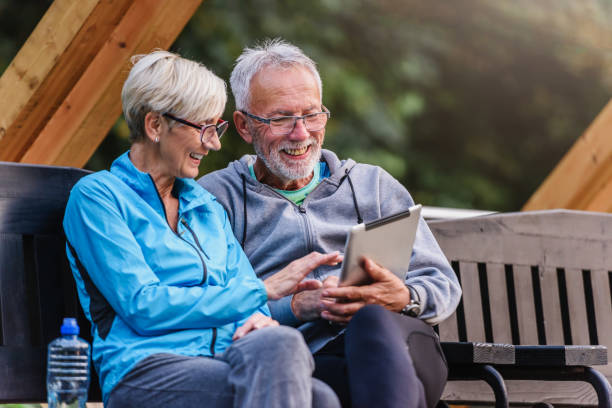 istock Smiling senior active couple sitting on the bench looking at tablet computer 1200131725