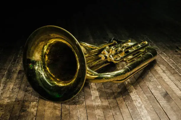 yellow brass instrument lies on a wooden floor in the dark