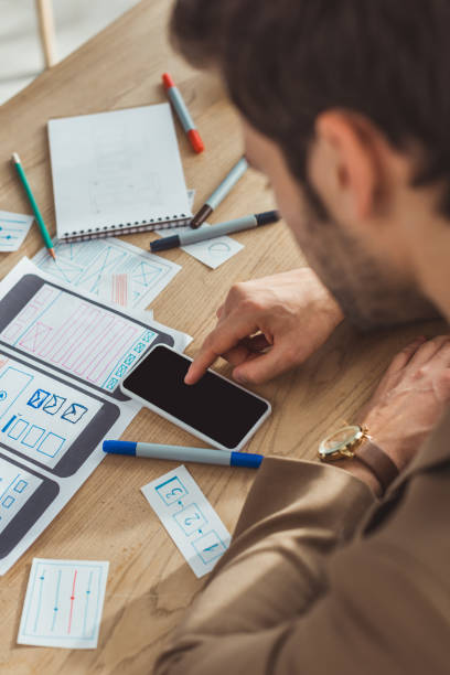 istock Selective focus of creative designer using smartphone by web sketches and layouts on table 1200140355