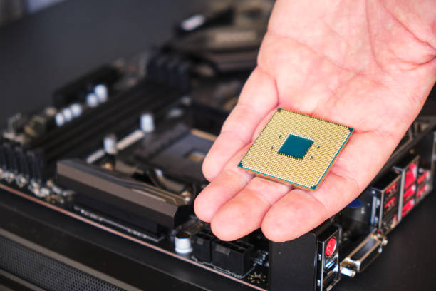 istock CPU (Central Processing Unit) held in a man's hand - close up, with a blurred motherboard in the background. Copy space. 1200141013