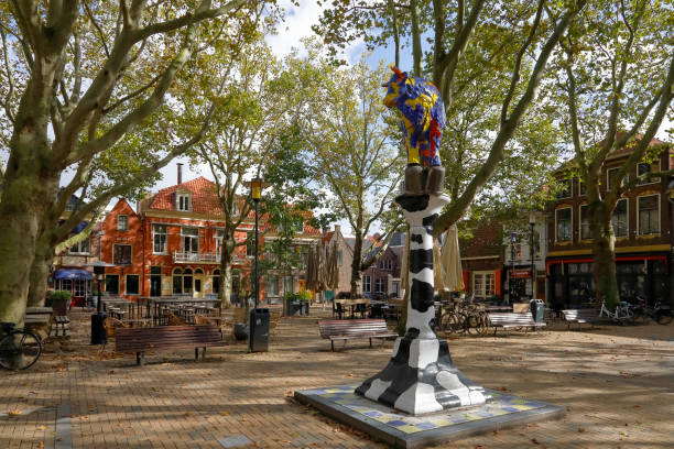 Delft, The Netherlands - October 10, 2019: Here is the Beestenmarkt square in the middle of which there is a colorful cow statue. Delft is a popular tourist destination. Many tourists come here and find in this city a summary of the architecture, art and landscape of the Netherlands. Many historical buildings have been preserved in the old part of the city. There are many narrow streets and many of them are canals, the banks of which are connected by small bridges. The city is known for its connections to art, culture and science.