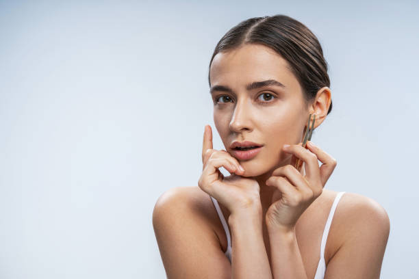 istock Charming tender girl using tweezers against light background 1200145658